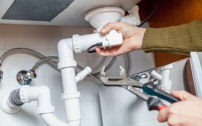 Someone Holding A Wrench Unscrewing A Pipe Underneath A Bathroom Sink.