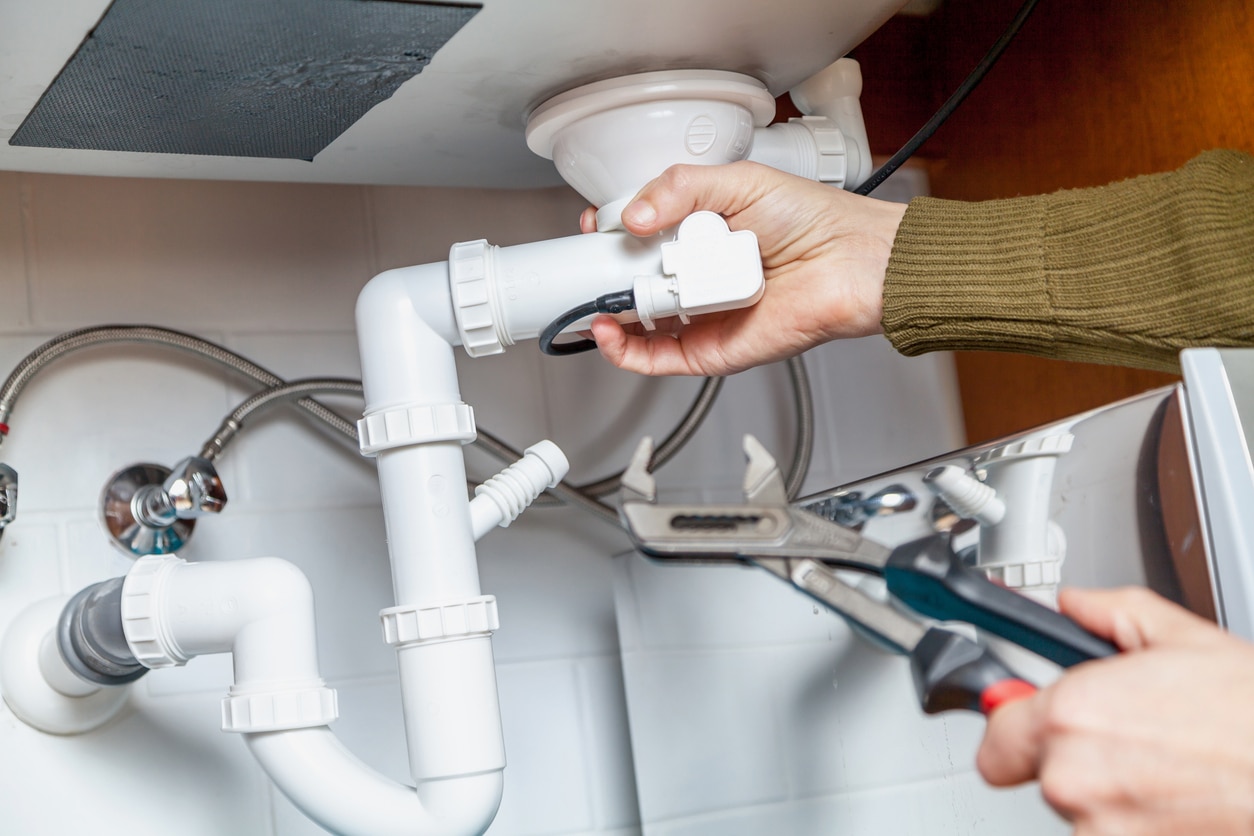 Someone holding a wrench unscrewing a pipe underneath a bathroom sink.