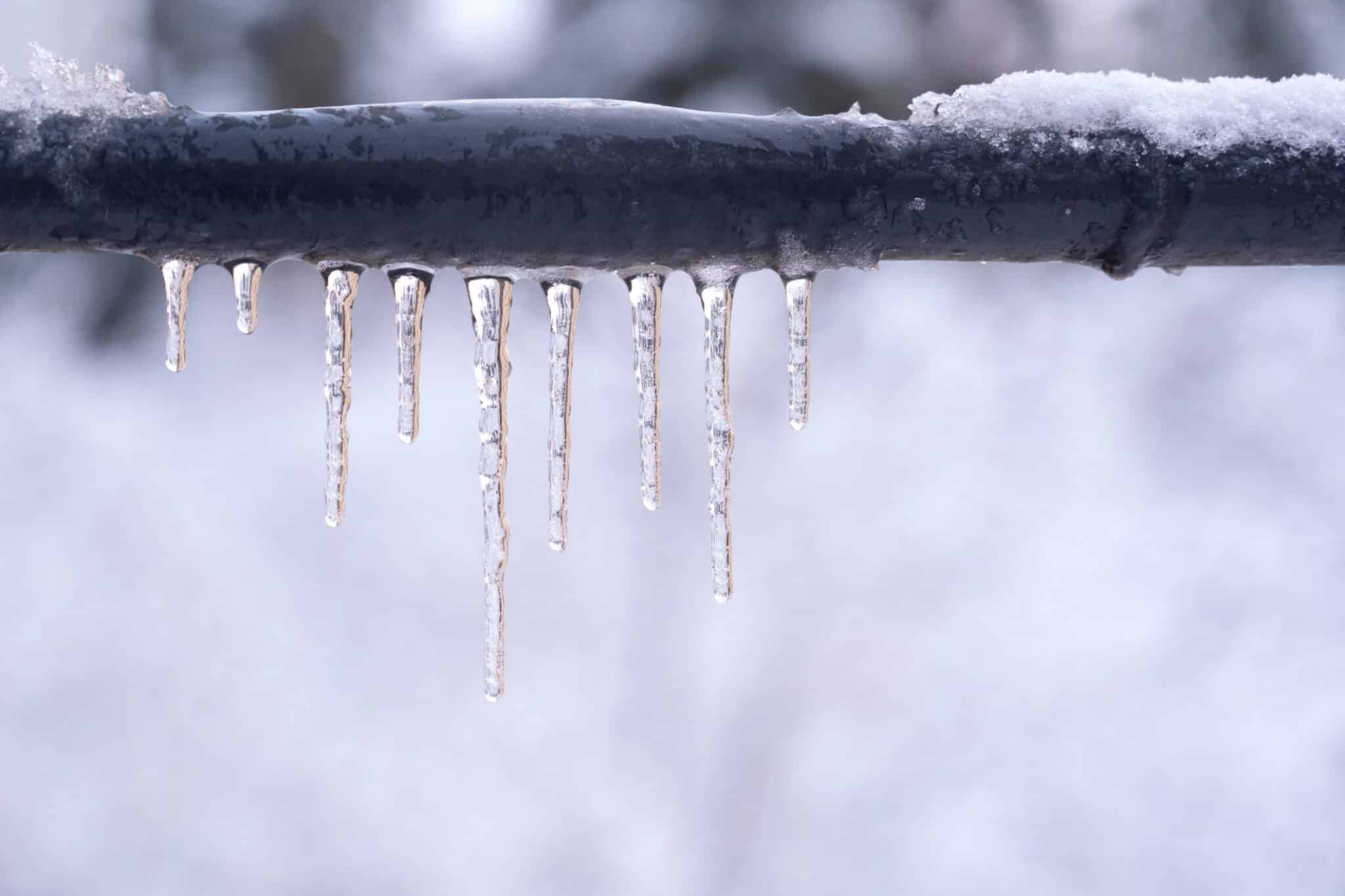 A frozen pipe during a snowy day, dripping with icicles.